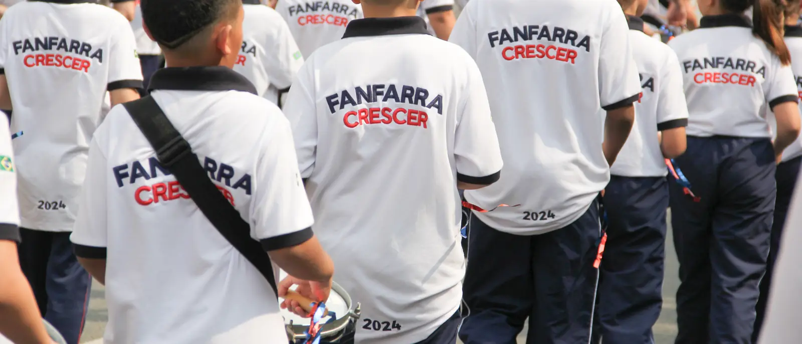 Alunos da Fanfarra Crescer de costas, com a camiseta da Fanfarra, durante o desfile de 7 de setembro